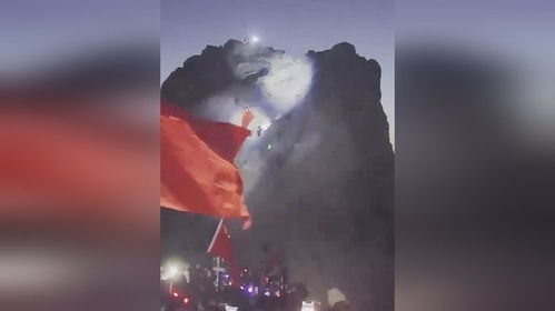 一名男子在山顶举起国旗身后是众人用手电照亮的光点