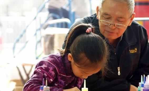 刘爷爷坐在老屋前操控布袋戏木偶