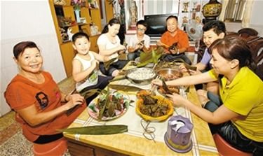 一家人围坐在餐桌旁包粽子的场景